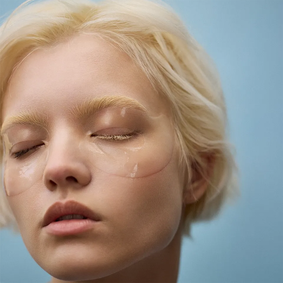 Woman wearing In My Eyes eye patches (eye mask) for sensitive dry eyes, hydrating skincare on a blue background.